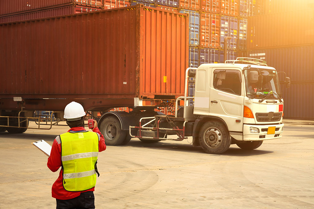 A foreman directing a truck with a container truck