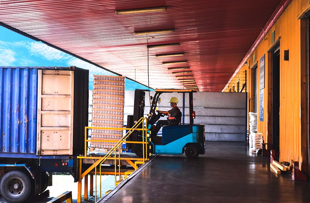 A forklift unloading a container truck at a loading dock